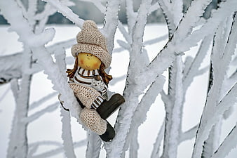 Cute knitted doll sitting on snowy tree branch in winter