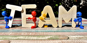 Colorful figurines holding wooden TEAM letters on rustic table