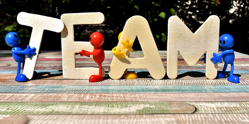 Colorful figurines holding wooden TEAM letters on rustic table