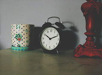 Vintage alarm clock, floral mug, and red lamp on a table