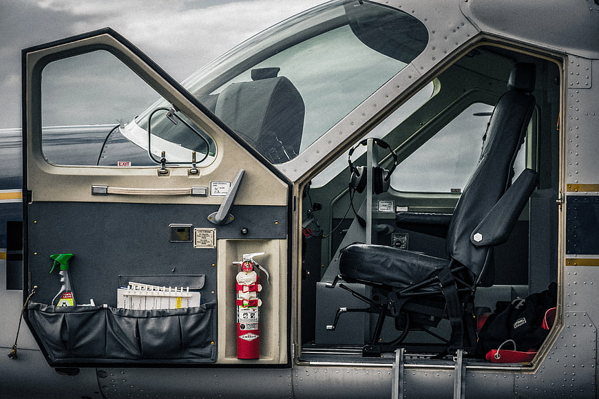 Open helicopter cockpit door with pilot seat and fire extinguisher