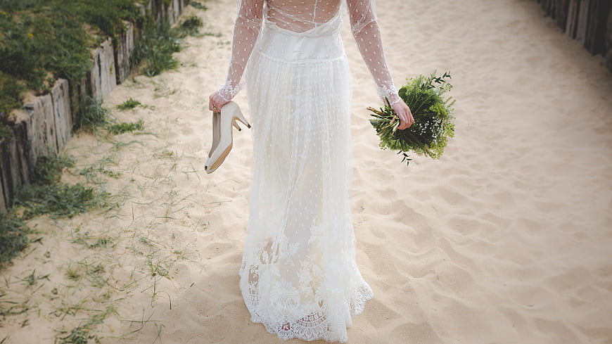Bride in Lace Wedding Dress Walking on Sandy Beach