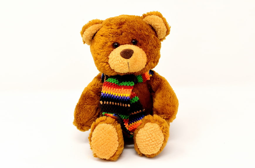 Brown Teddy Bear Wearing Colorful Knitted Scarf on White Background