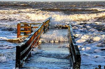 Storm waves crashing over wooden pier railing