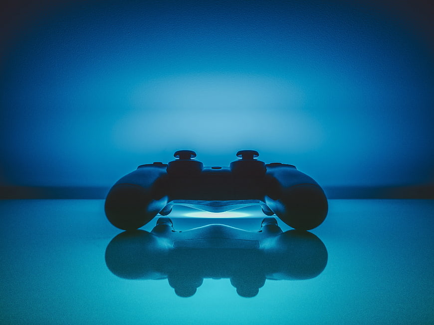 Silhouette of a video game controller on a reflective surface with blue neon lighting