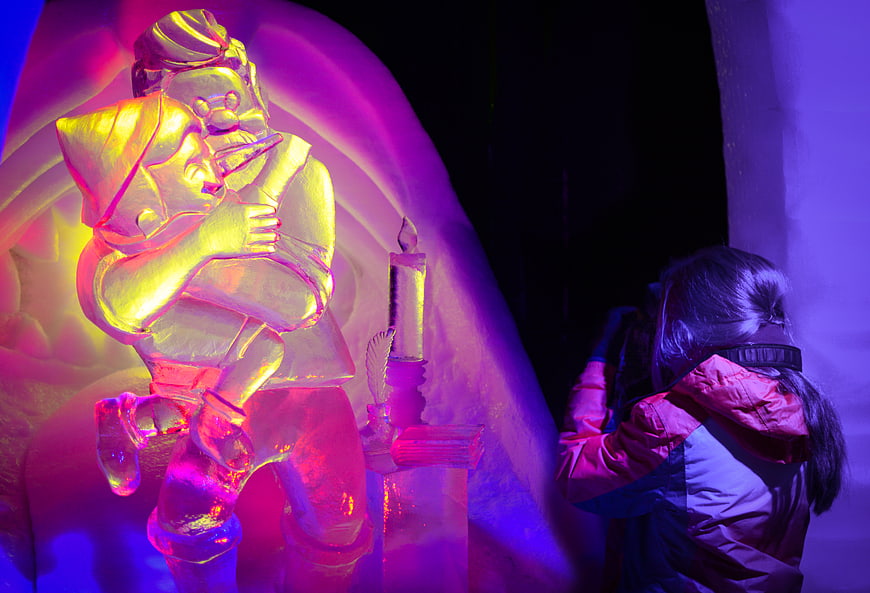 Child photographing colorful ice sculpture at winter festival
