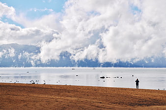 Lone figure standing on sandy beach with mountains and clouds