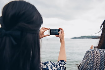 Two women taking photos of the sea with smartphones