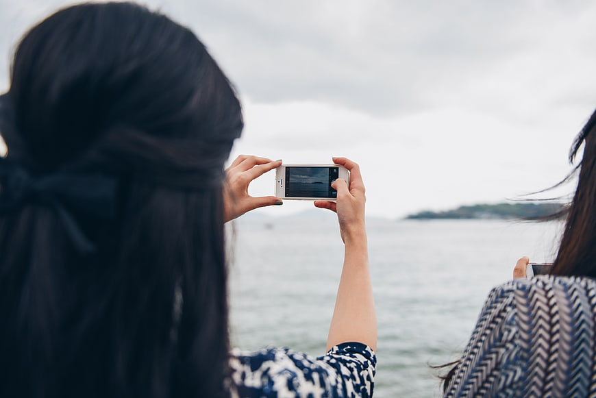 Two women taking photos of the sea with smartphones