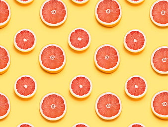Flat lay pattern of sliced grapefruits on yellow background