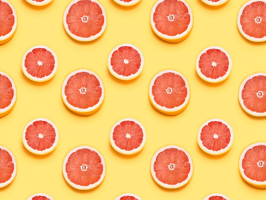 Flat lay pattern of sliced grapefruits on yellow background
