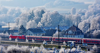 Red train passing through frosty winter village landscape