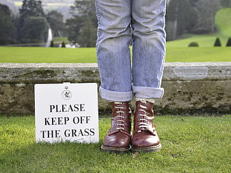 Person in brown boots standing on grass next to keep off sign