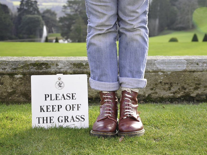 Person in brown boots standing on grass next to keep off sign