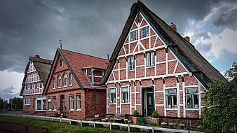 Traditional Half-Timbered Houses with Thatched Roof Under Stormy Sky