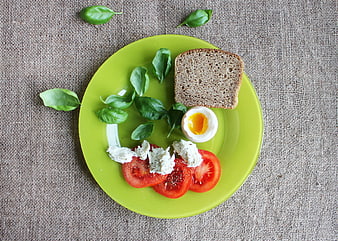 Healthy breakfast with tomatoes, egg, and bread on green plate