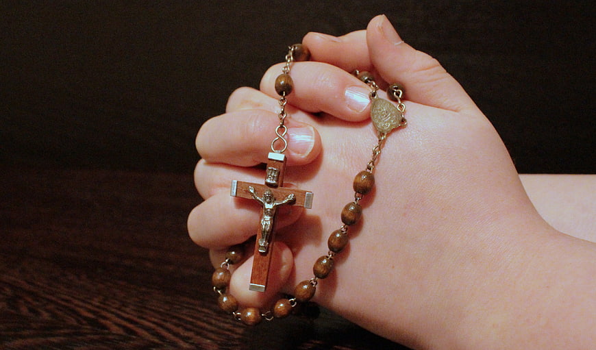 Hand holding wooden rosary beads and crucifix in prayer