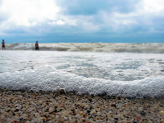 Close-up of sea foam on pebbly beach with blurred waves
