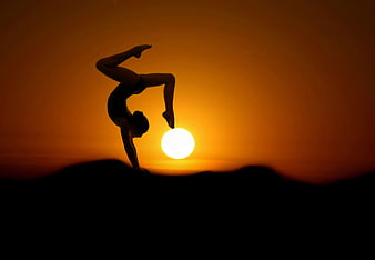 Silhouette of a woman performing a yoga handstand against a sunset