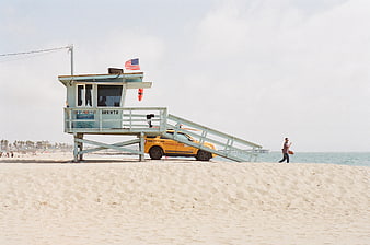 Lifeguard tower and yellow SUV on sandy beach with American flag