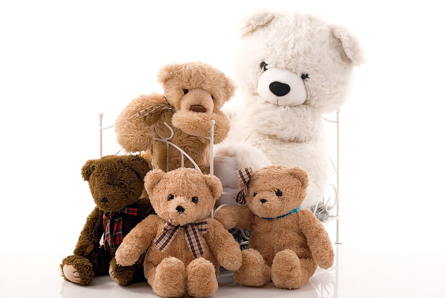 Group of teddy bears sitting on a white metal bed frame