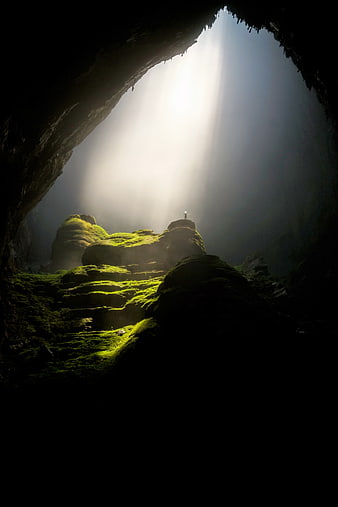 Silhouette of person standing in mossy cave with light rays