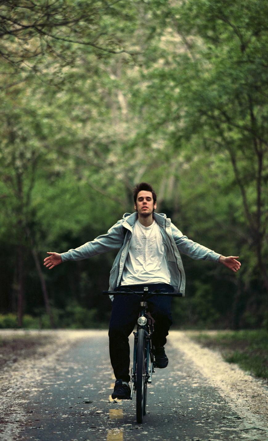 Young Man Riding Bicycle No Hands on Forest Road