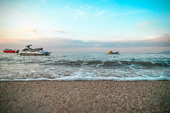 Low angle beach view with jet skis in ocean at sunset