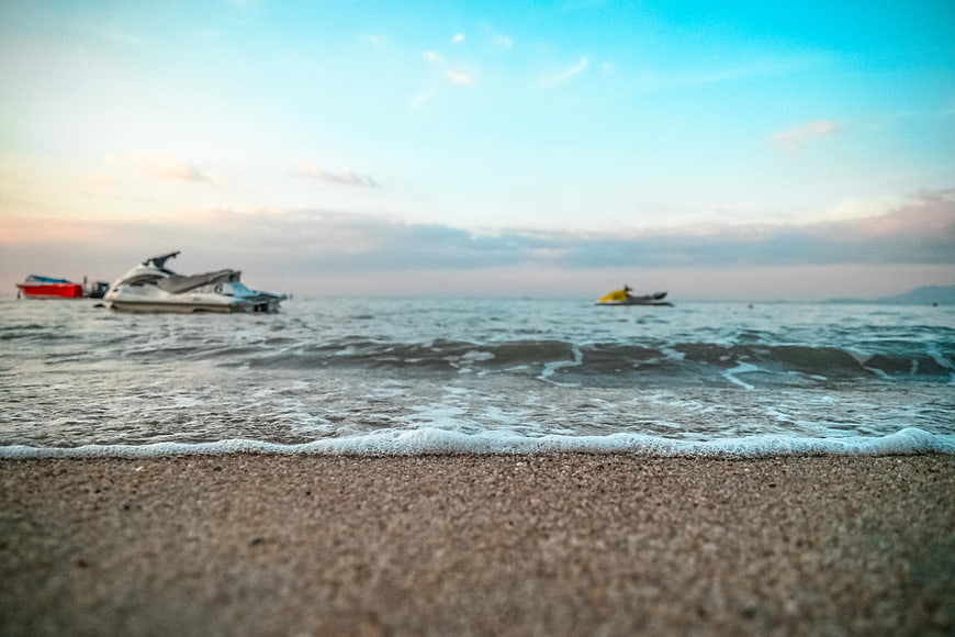 Low angle beach view with jet skis in ocean at sunset