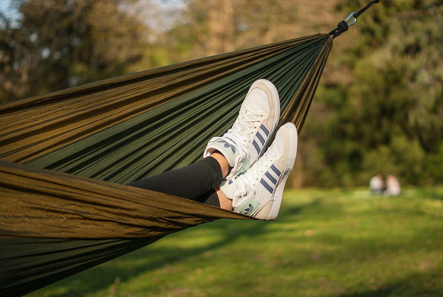 White Sneakers And Legs Relaxing In Green Outdoor Hammock