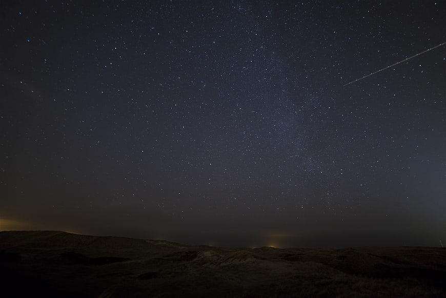 Starry Night Sky with Satellite Trail over Dark Landscape