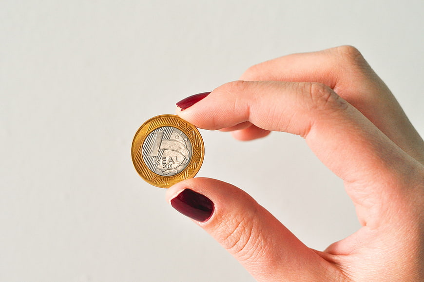 Hand holding Brazilian 1 Real coin on white background