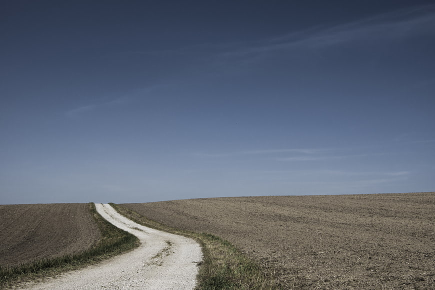 Winding gravel road through dry agricultural fields under blue sky