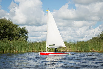 Red and white sailboat gliding through calm river waters