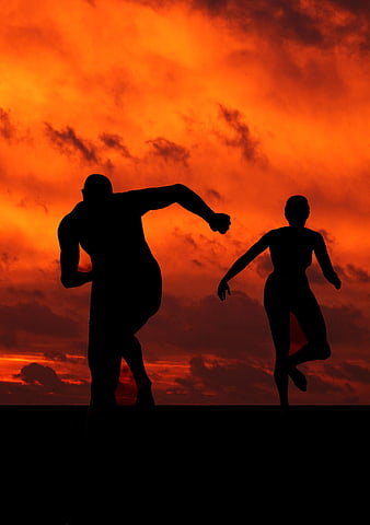 Silhouette of male and female runners sprinting against fiery sunset