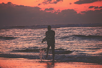 Silhouette of man splashing in ocean at sunset