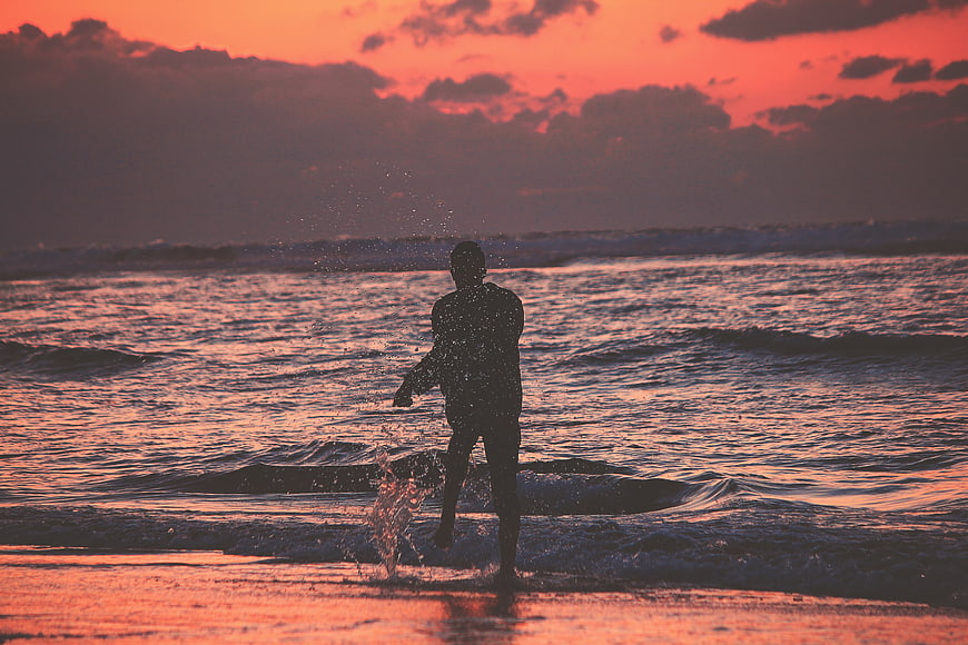 Silhouette of man splashing in ocean at sunset