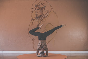 Woman performing headstand yoga pose in front of artistic wall mural