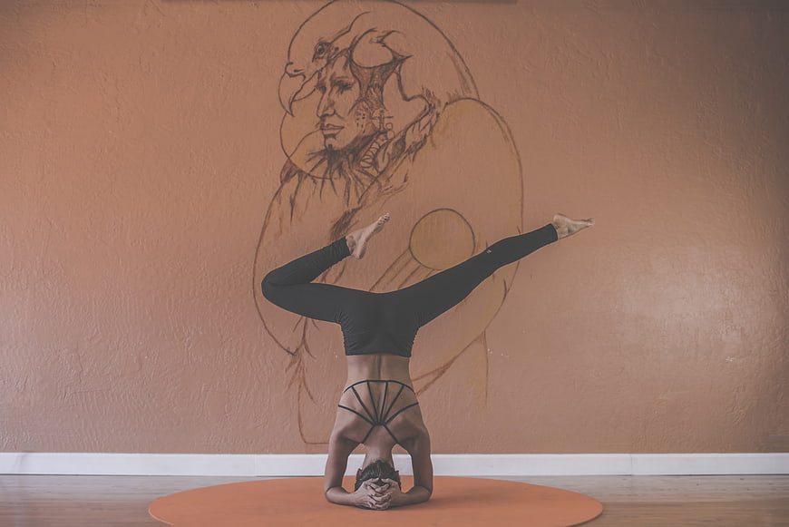 Woman performing headstand yoga pose in front of artistic wall mural