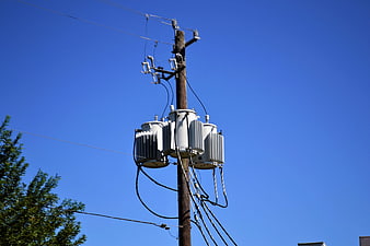 Wooden utility pole with three-phase transformer against clear blue sky