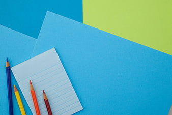 Colorful pencils and notepad on blue and green paper background