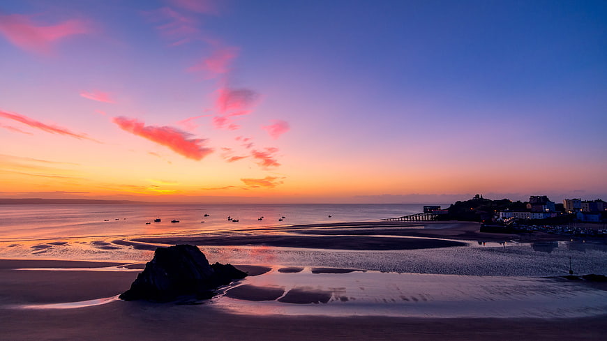 Colorful Sunset Over Tenby Beach with Silhouetted Rock and Pier