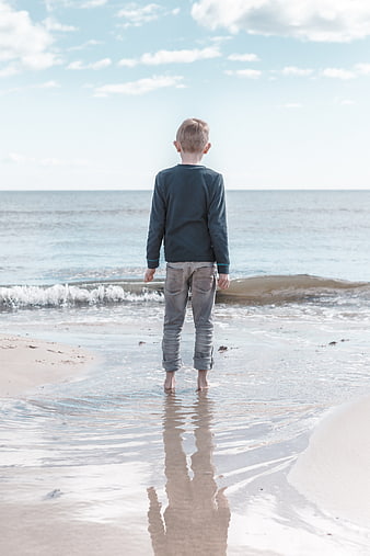 Young Boy Standing on Beach Looking at Ocean