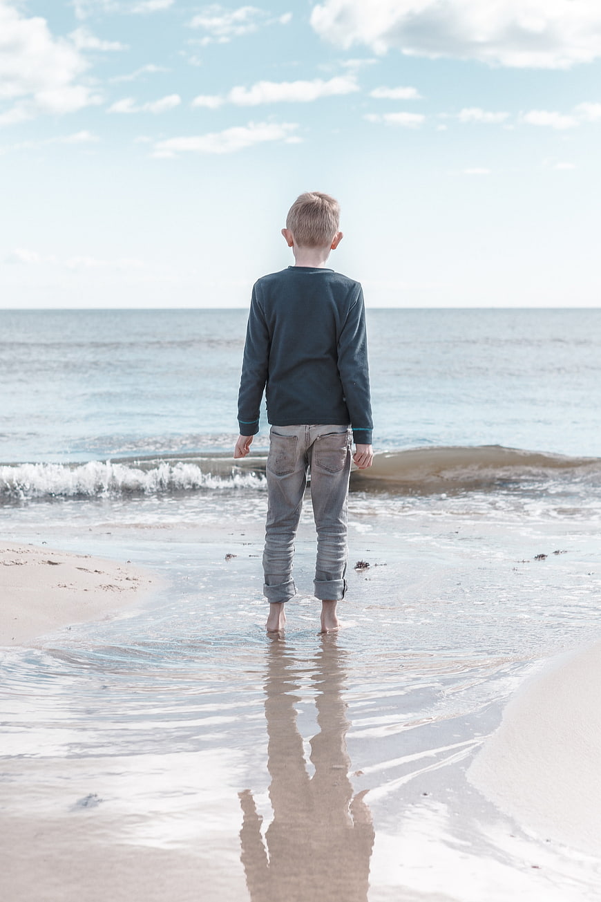 Young Boy Standing on Beach Looking at Ocean