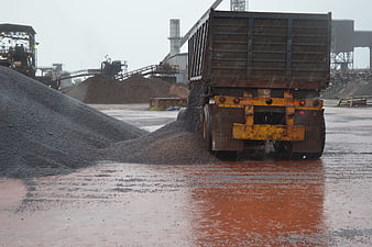 Dump truck unloading gravel at industrial plant in rain