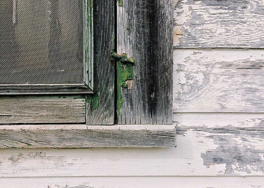 Weathered wooden window with peeling paint on rustic cabin exterior