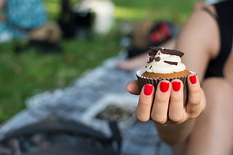 Hand holding chocolate cupcake with red nails outdoors