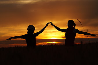 Silhouette of mother and child making heart shape at sunset