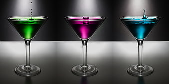 Three colorful cocktails in martini glasses with splashing drops
