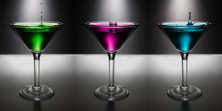 Three colorful cocktails in martini glasses with splashing drops